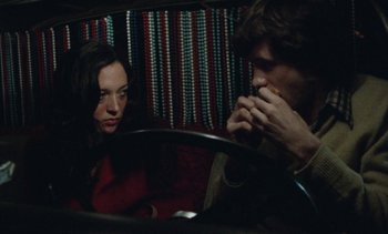 Movie still from “Smithereens” (1982), directed by Susan Seidelman – A man and a woman sitting in front of a steering wheel; Medium shot, High angle