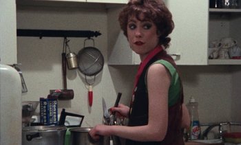 Movie still from “Smithereens” (1982), directed by Susan Seidelman – A woman standing in a kitchen holding a pan; Close Up shot, Over the shoulder angle