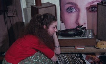 Movie still from “Smithereens” (1982), directed by Susan Seidelman – A woman sitting on top of a record player next to some records; Medium shot, High angle