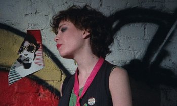 Movie still from “Smithereens” (1982), directed by Susan Seidelman – A young woman with curly brown hair wearing a black shirt; Close Up shot, Over the shoulder angle