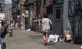 Movie still from “Smithereens” (1982), directed by Susan Seidelman – A woman walking down the street with a bag of trash; Wide shot, High angle