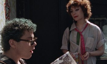 Movie still from “Smithereens” (1982), directed by Susan Seidelman – A woman standing next to a man holding a book; Medium shot, Over the shoulder angle
