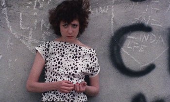 Movie still from “Smithereens” (1982), directed by Susan Seidelman – A woman in a white and black polka dot dress is leaning against a wall; Close Up shot, Overhead angle