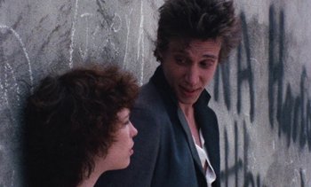 Movie still from “Smithereens” (1982), directed by Susan Seidelman – A man and a woman standing next to each other; Close Up shot, Over the shoulder angle