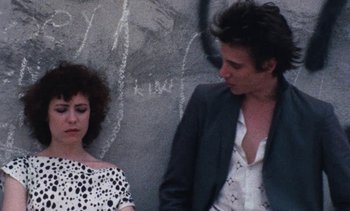 Movie still from “Smithereens” (1982), directed by Susan Seidelman – A man and a woman standing next to each other in front of a wall; Close Up shot, Over the shoulder angle