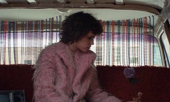 Movie still from “Smithereens” (1982), directed by Susan Seidelman – A woman in a pink coat sitting on a chair; Medium shot, High angle