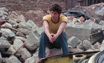 Movie still from “Smithereens” (1982), directed by Susan Seidelman – A man sitting on the ground in the middle of a pile of rubble; Medium shot, High angle