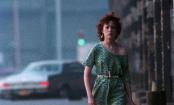 Movie still from “Smithereens” (1982), directed by Susan Seidelman – A woman in a green dress walking down a street; Medium shot, Over the shoulder angle