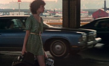 Movie still from “Smithereens” (1982), directed by Susan Seidelman – A woman walking down the street with a camera; Wide shot, Over the shoulder angle