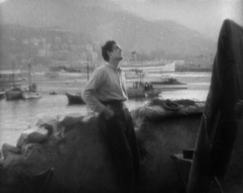 Movie still from “Street Angel” (1928), directed by Frank Borzage – A black and white photo of a man sitting on a rock; Wide shot, High angle