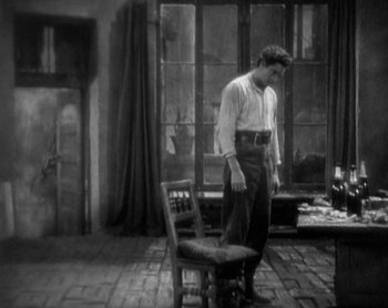 Movie still from “Street Angel” (1928), directed by Frank Borzage – A black and white photo of a man standing next to a chair; Wide shot, High angle