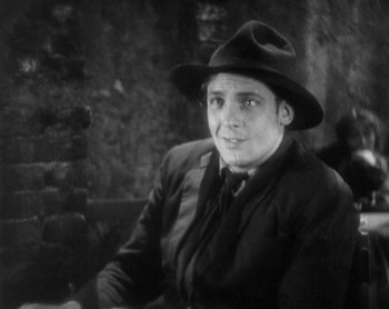 Movie still from “Street Angel” (1928), directed by Frank Borzage – A man wearing a hat sitting in front of a brick wall; Close Up shot, Low angle