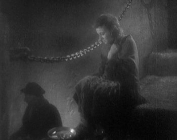 Movie still from “Street Angel” (1928), directed by Frank Borzage – A woman sitting on a chair in a dark room next to a man; Wide shot, High angle