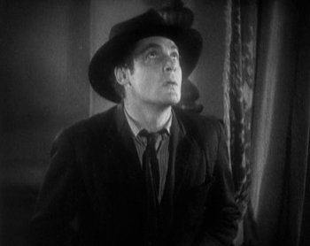 Movie still from “Street Angel” (1928), directed by Frank Borzage – A black and white photo of a man wearing a suit and a hat; Close Up shot, Low angle