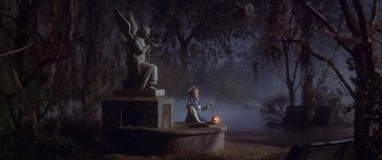 A little girl sitting on top of a statue holding a pumpkin
