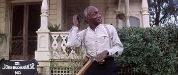 Movie still from “Summer and Smoke” (1961), directed by Peter Glenville – An older man is holding a baseball bat in front of a house; Medium shot, Low angle
