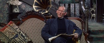Movie still from “Summer and Smoke” (1961), directed by Peter Glenville – An older man sitting on a couch holding a book; Medium shot, Low angle