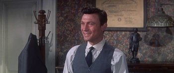 Movie still from “Summer and Smoke” (1961), directed by Peter Glenville – A man in a vest and tie smiling for the camera; Medium shot, Over the shoulder angle