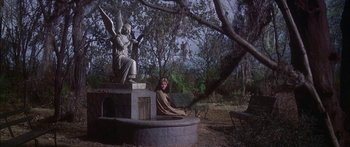 Movie still from “Summer and Smoke” (1961), directed by Peter Glenville – A statue of an angel sitting on top of a bench next to a woman; Wide shot, High angle