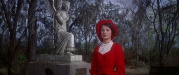 Movie still from “Summer and Smoke” (1961), directed by Peter Glenville – A woman in a red dress standing in front of a statue; Medium shot, Low angle