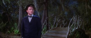 Movie still from “Summer and Smoke” (1961), directed by Peter Glenville – A man in a suit and hat standing in front of a forest; Medium shot, Low angle