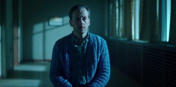 Movie still from “Fargo” (2014), created by Noah Hawley – A man wearing a blue sweater sitting in a dark room; Medium shot, Low angle