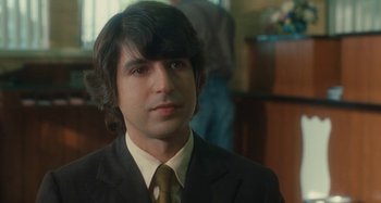 Movie still from “Taking Woodstock” (2009), directed by Ang Lee – A man in a suit and tie in front of a counter; Close Up shot, Over the shoulder angle
