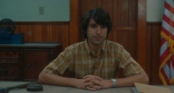 Movie still from “Taking Woodstock” (2009), directed by Ang Lee – A man sitting at a table with his hands crossed; Medium shot, High angle