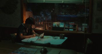 Movie still from “Taking Woodstock” (2009), directed by Ang Lee – A person sitting at a table writing on a piece of paper; Medium shot, Low angle