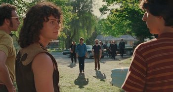 Movie still from “Taking Woodstock” (2009), directed by Ang Lee – A group of people standing on top of a grass covered field; Medium shot, Over the shoulder angle
