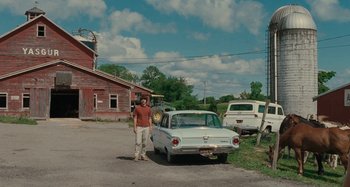 Movie still from “Taking Woodstock” (2009), directed by Ang Lee – A man standing next to an old car in a parking lot; Wide shot, Low angle