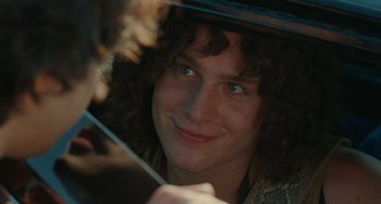 Movie still from “Taking Woodstock” (2009), directed by Ang Lee – A man with curly brown hair is smiling at the camera; Close Up shot, Over the shoulder angle