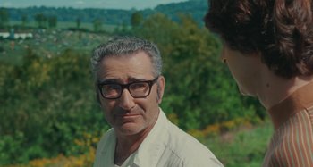 Movie still from “Taking Woodstock” (2009), directed by Ang Lee – An older man wearing glasses and a white shirt; Close Up shot, Over the shoulder angle
