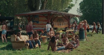 Movie still from “Taking Woodstock” (2009), directed by Ang Lee – A group of people sitting in the grass near a gazebo; Wide shot, High angle