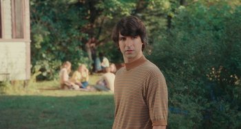 Movie still from “Taking Woodstock” (2009), directed by Ang Lee – A young man standing in front of a group of people in a park; Medium shot, Over the shoulder angle