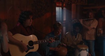 Movie still from “Taking Woodstock” (2009), directed by Ang Lee – A group of people sitting in a room with a guitar; Medium shot, Over the shoulder angle