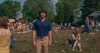 Movie still from “Taking Woodstock” (2009), directed by Ang Lee – A man standing in a field with people sitting in the background; Medium shot, Over the shoulder angle