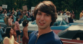 A young man with brown hair standing in front of a crowd of onlookers