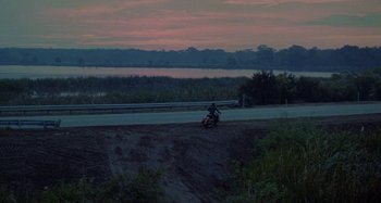 Movie still from “The Loveless” (1981), directed by Kathryn Bigelow – A person riding a motorcycle down a dirt road; Extreme Wide shot, High angle