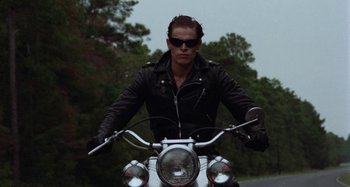 Movie still from “The Loveless” (1981), directed by Kathryn Bigelow – A man wearing a black leather jacket on a motorcycle; Medium shot, Low angle