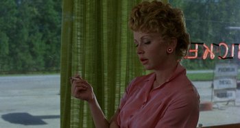 Movie still from “The Loveless” (1981), directed by Kathryn Bigelow – A woman in a pink shirt is smoking a cigarette; Close Up shot, Low angle