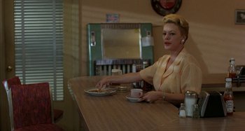 Movie still from “The Loveless” (1981), directed by Kathryn Bigelow – A woman sitting at a table with a plate of food in front of her; Medium shot, Over the shoulder angle