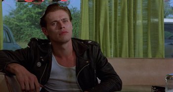 Movie still from “The Loveless” (1981), directed by Kathryn Bigelow – A man wearing a leather jacket sitting on a couch; Close Up shot, Low angle