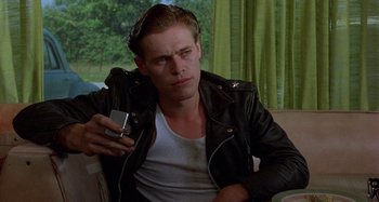 Movie still from “The Loveless” (1981), directed by Kathryn Bigelow – A man in a black leather jacket holding a cell phone; Close Up shot, Low angle
