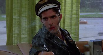 Movie still from “The Loveless” (1981), directed by Kathryn Bigelow – A man in a leather jacket and hat smoking a cigarette; Close Up shot, Low angle