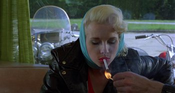 Movie still from “The Loveless” (1981), directed by Kathryn Bigelow – A woman with blonde hair is lighting a cigarette; Close Up shot, Low angle