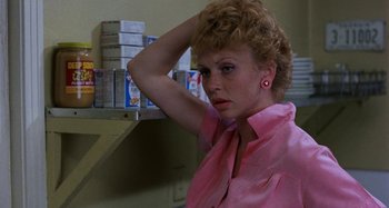Movie still from “The Loveless” (1981), directed by Kathryn Bigelow – A woman in a pink shirt is standing in front of a counter; Close Up shot, Low angle