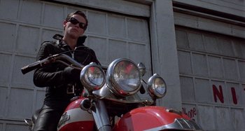 Movie still from “The Loveless” (1981), directed by Kathryn Bigelow – A man sitting on a red and white motorcycle; Medium shot, Low angle