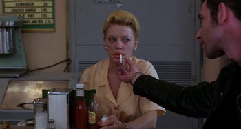 Movie still from “The Loveless” (1981), directed by Kathryn Bigelow – A woman sitting at a table with a cigarette in her mouth; Close Up shot, Over the shoulder angle