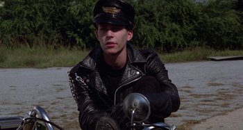 Movie still from “The Loveless” (1981), directed by Kathryn Bigelow – A man in a leather jacket and hat sitting on a motorcycle; Medium shot, High angle